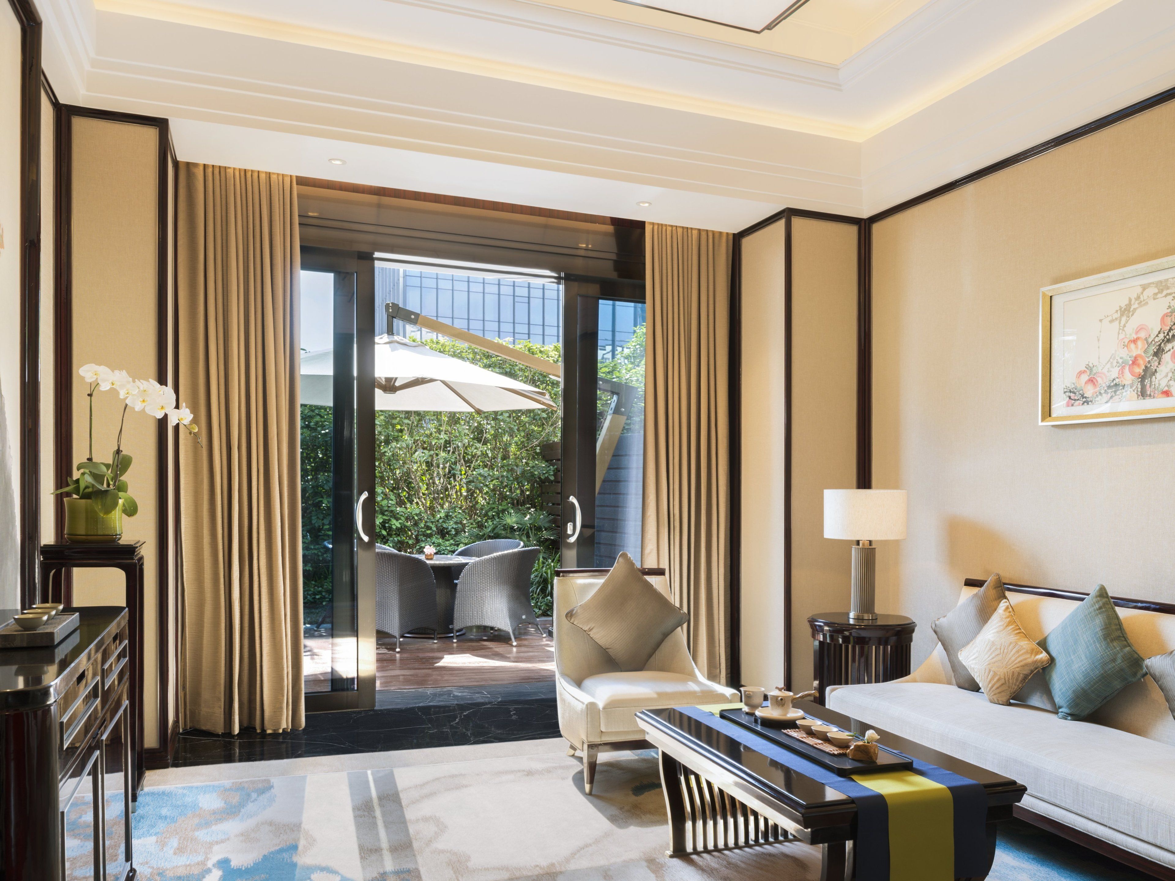 A hotel room with a sofa, a chair, a table, a lamp, and a view of the outdoors.