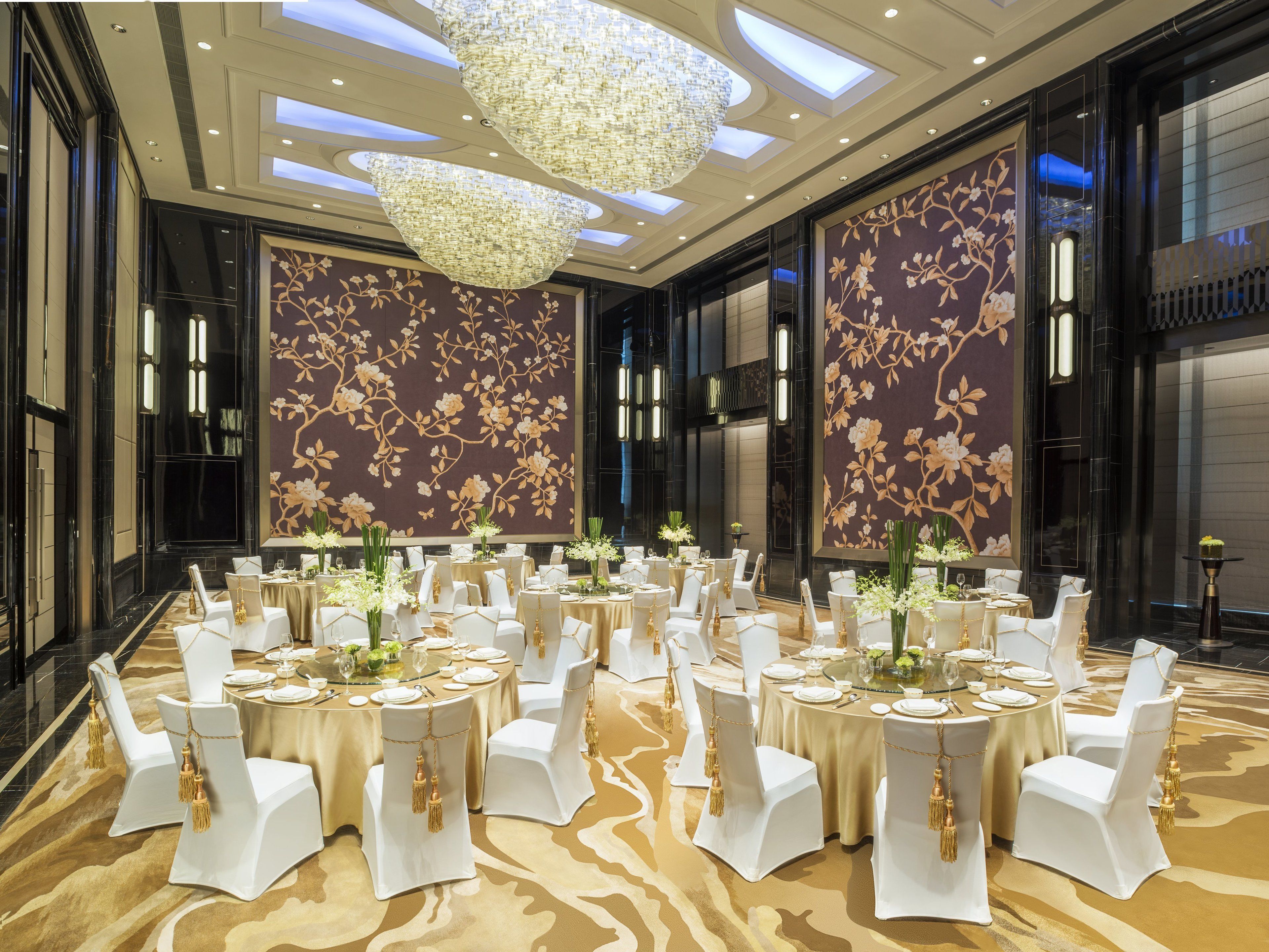 A banquet hall with round tables, white chairs, and floral wall decorations.