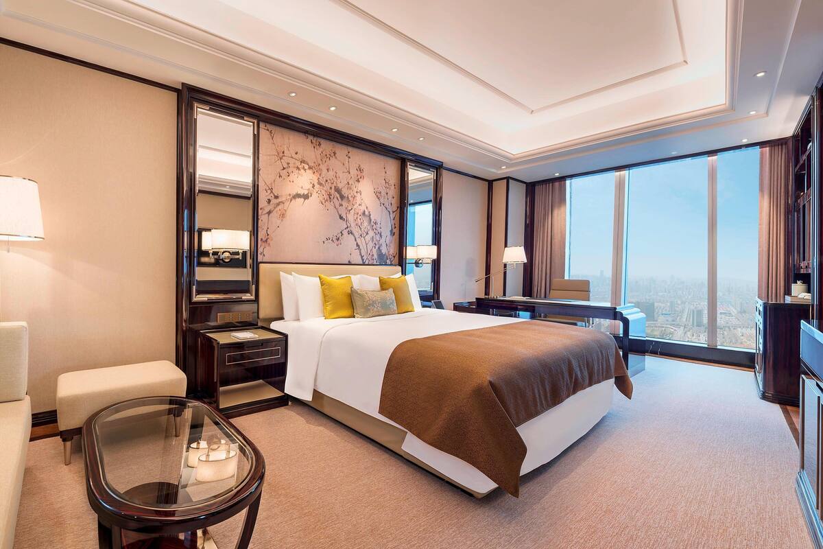 Ein modernes Hotelzimmer mit einem großen Bett, einem Glastisch, einer Sitzecke und Blick auf die Stadt.