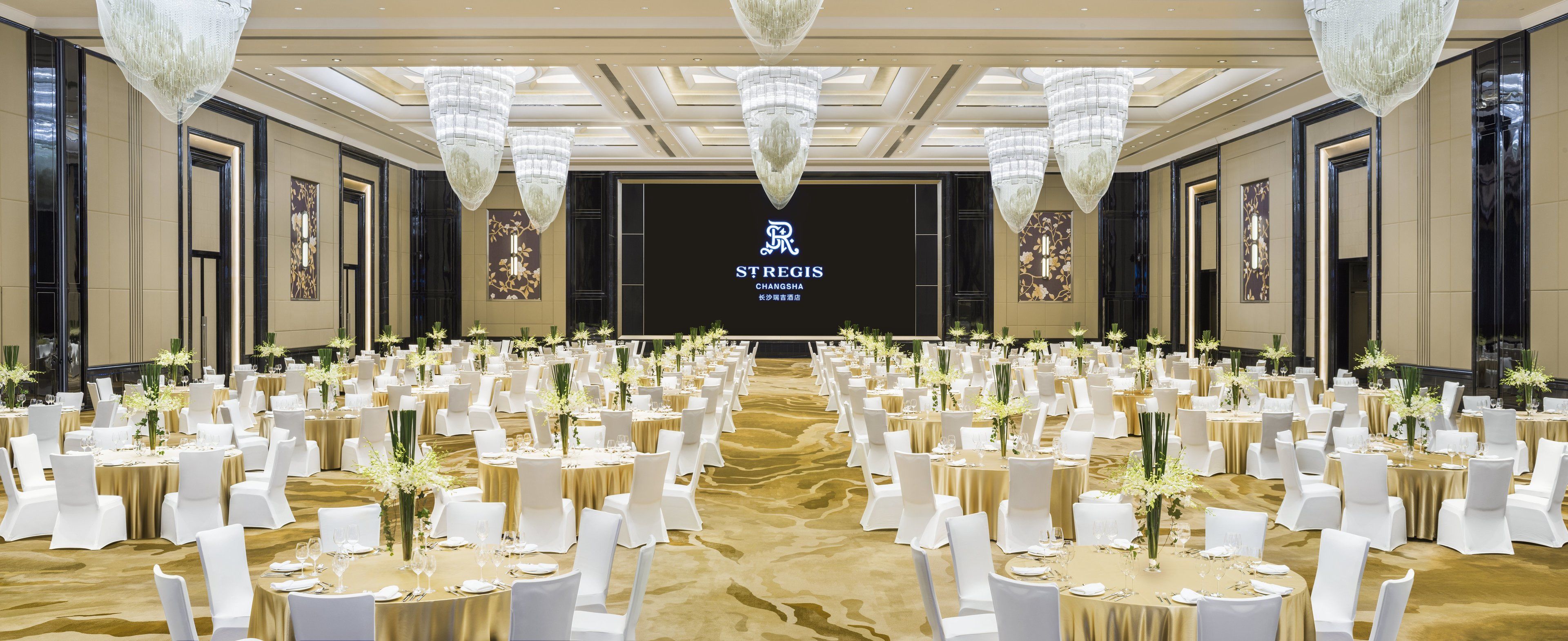 Une salle de banquet avec des tables rondes, des chaises blanches et des lustres.