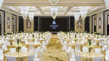 Une salle de banquet avec des tables rondes, des chaises blanches et des lustres.