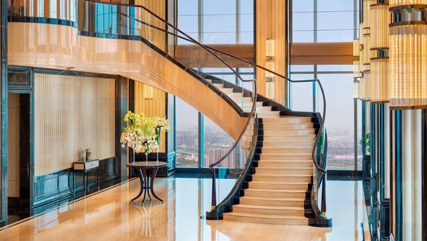 A grand staircase with a glass railing leading to an upper level, surrounded by large windows offering city views. - The St. Regis Changsha (Changsha)