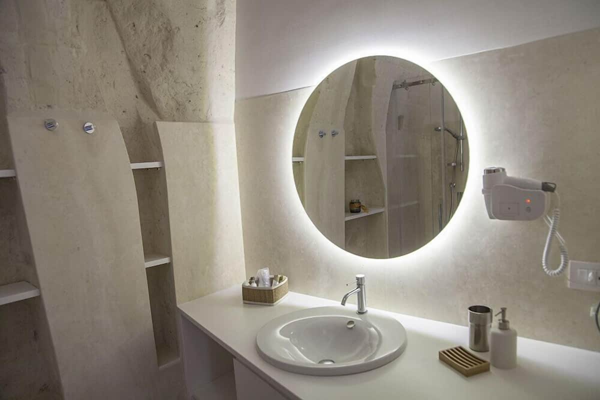 A modern bathroom with a round mirror, a sink, and a hairdryer on the wall.