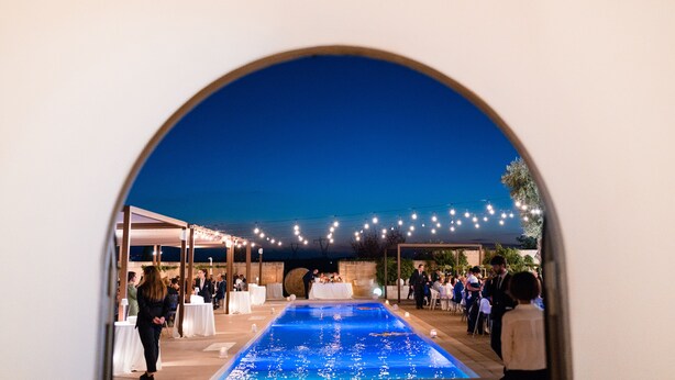 Un área de piscina al aire libre con zona de estar techada y luces colgantes.