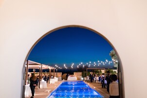 Area piscina all'aperto con zona relax coperta e luci decorative.