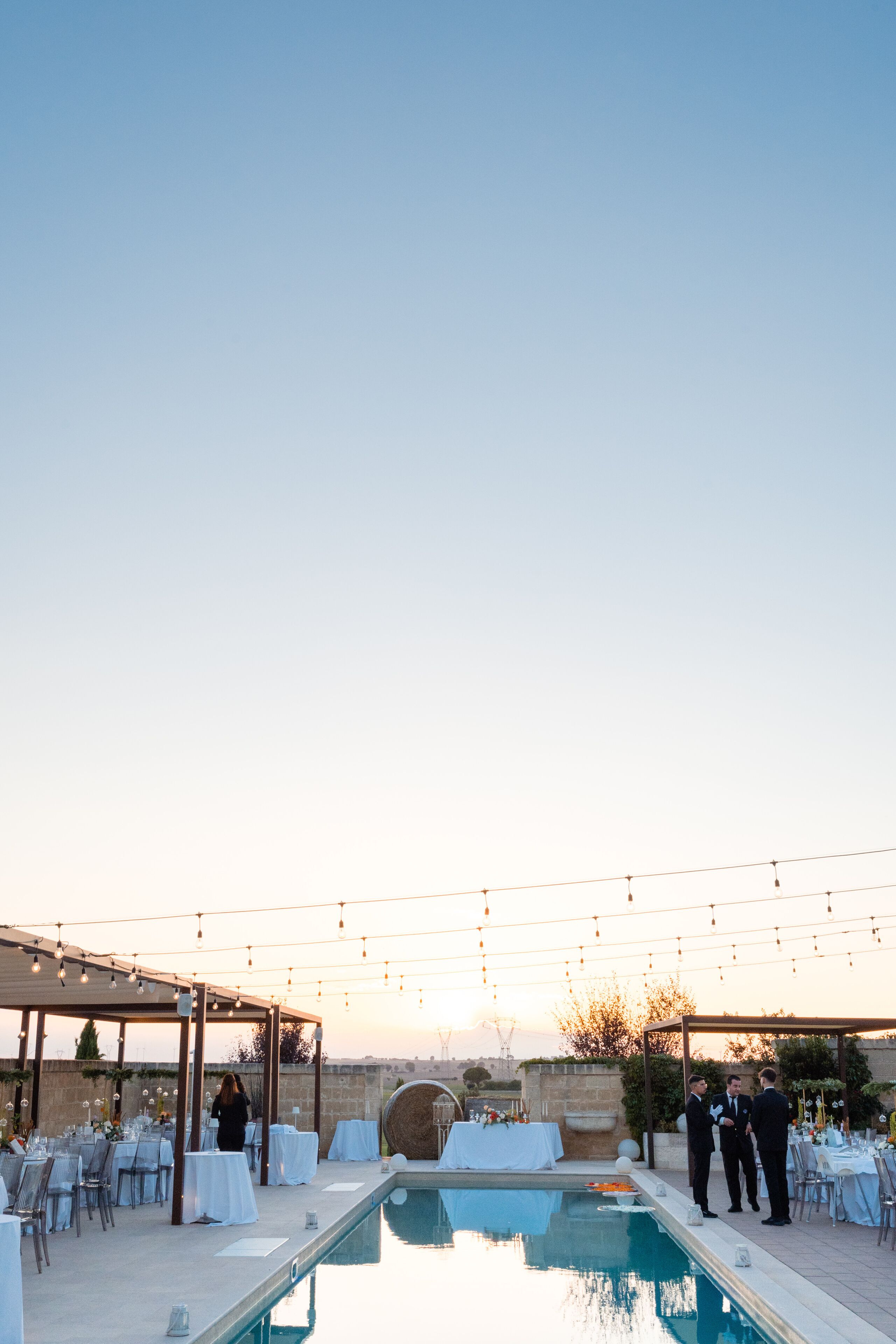 An outdoor wedding venue with a pool, tables set for guests, and string lights.
