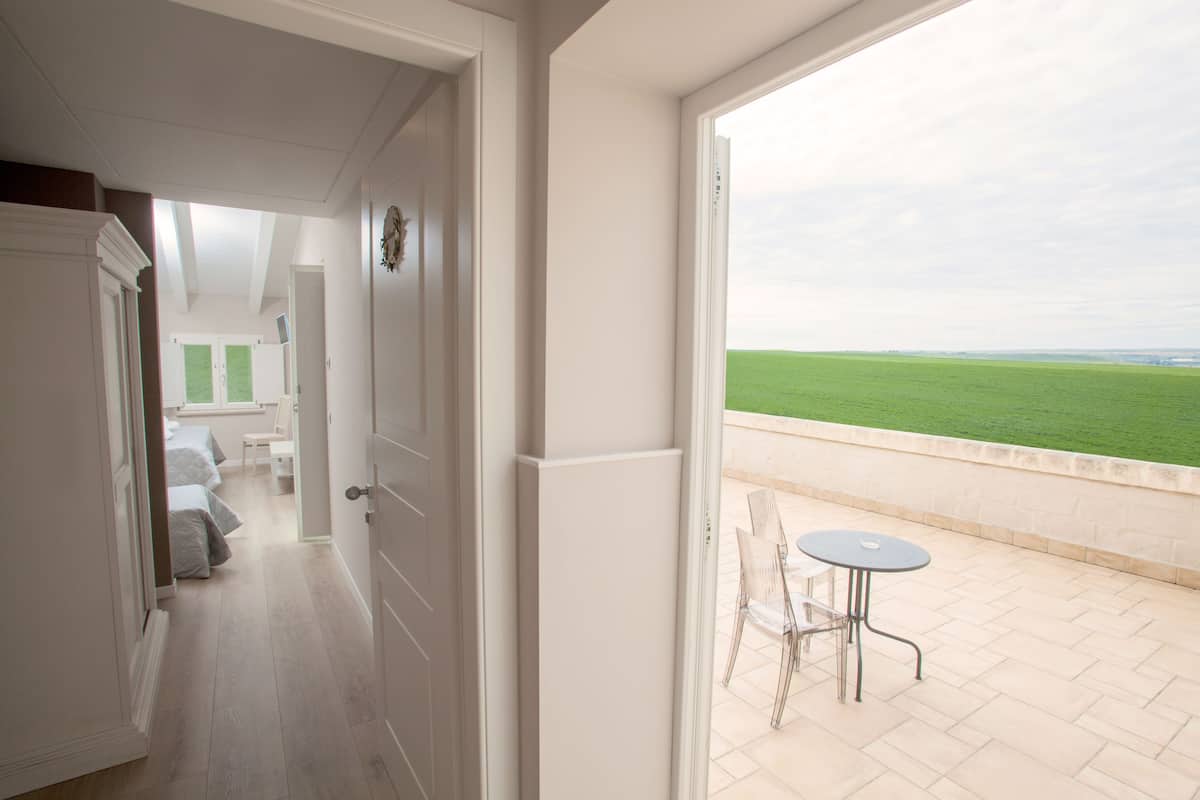 A corridor leading to a balcony with a view of a green field.