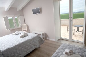 Una camera da letto con due letti, una TV a parete e un balcone con tavolo e sedie.