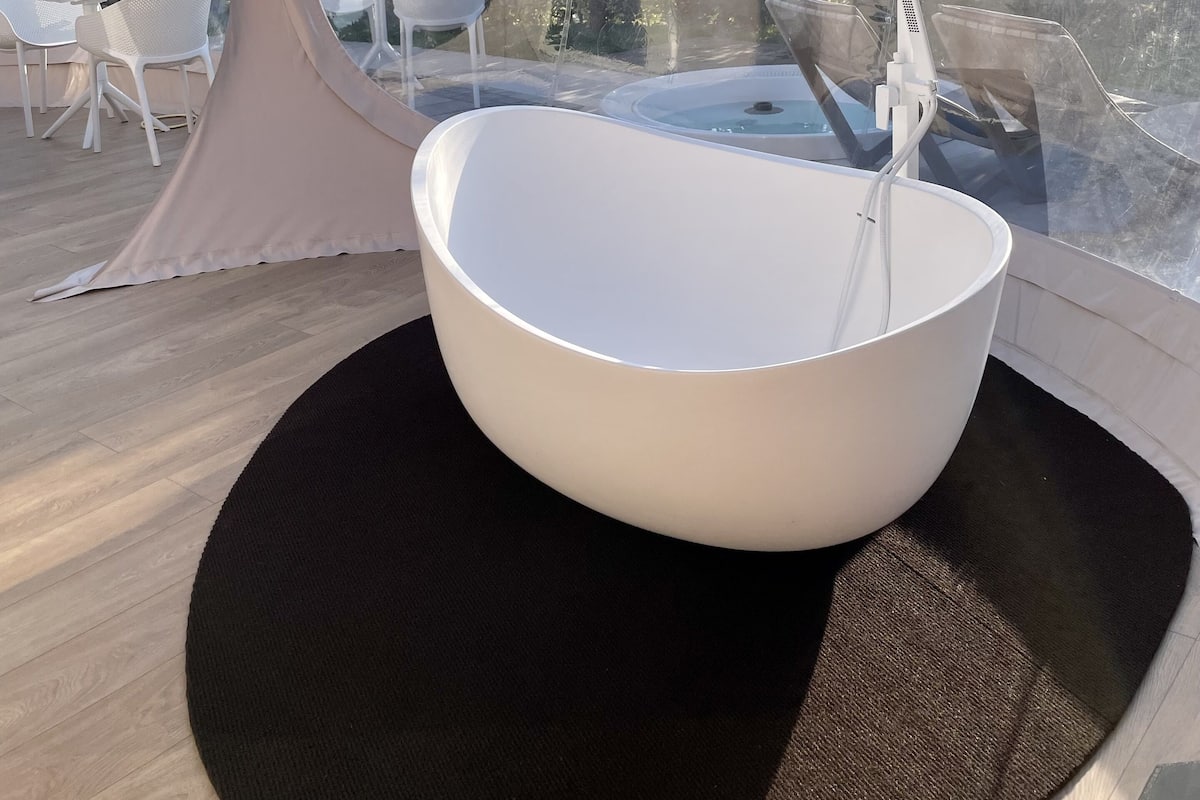 A modern bathroom with a large white bathtub, a black circular rug, and a glass-enclosed shower area.