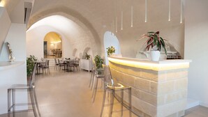 Un área de recepción moderna con mostrador de piedra, sillas transparentes y un comedor al fondo.
