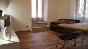 A modern living room with a wooden floor, a dining table with chairs, a sofa with cushions, and a staircase with a marble landing. - Una Finestra su Monti (Rome)