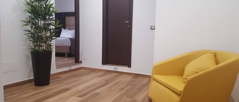 Une pièce avec un plancher en bois, un fauteuil jaune, une plante en pot et une porte fermée.