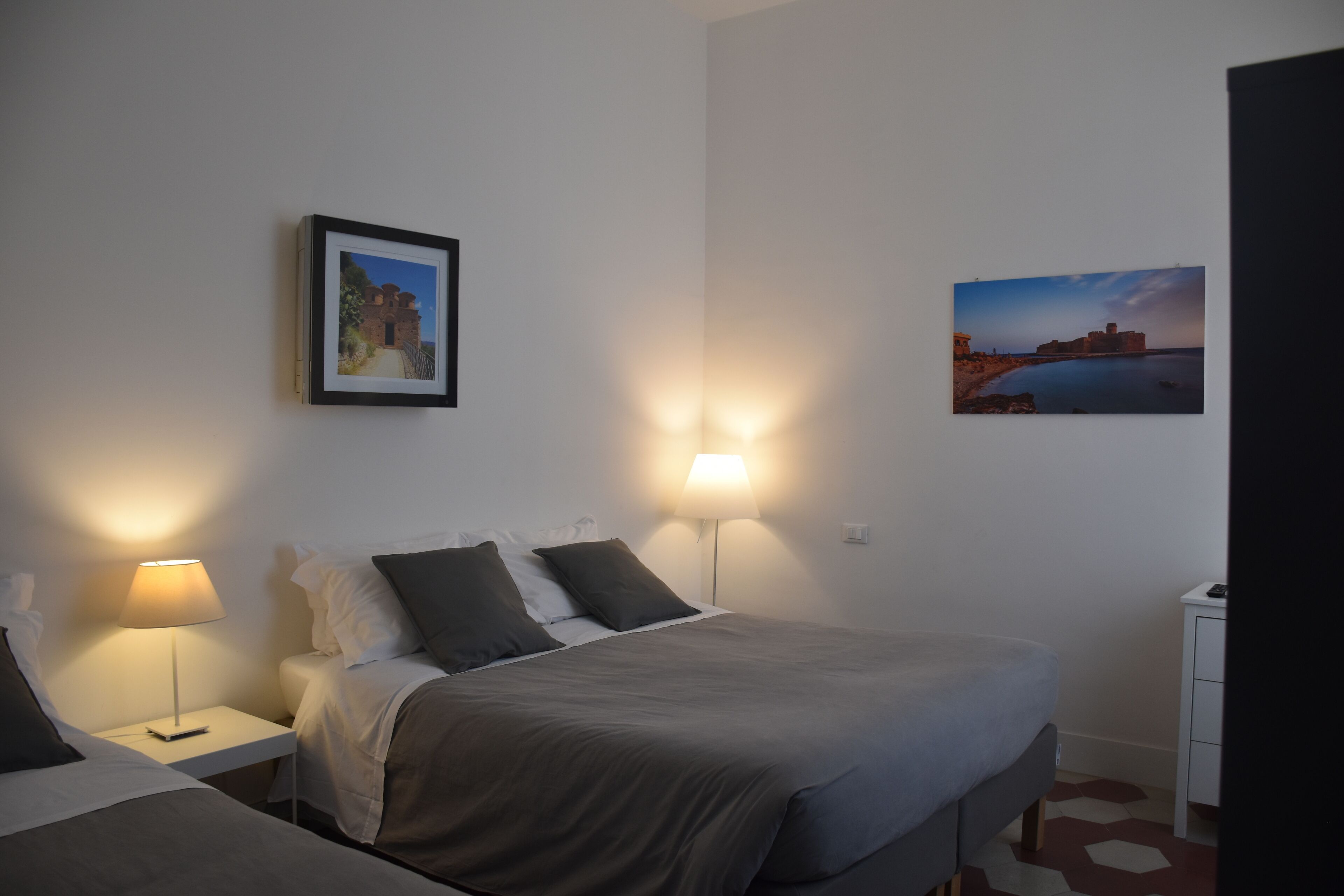 Una habitación de hotel con una cama, mesitas de noche, lámparas y dos cuadros en la pared.