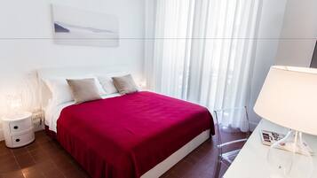 Quarto moderno com uma cama grande, roupa de cama branca, um cobertor vermelho e uma mesa de cabeceira com uma luminária.
