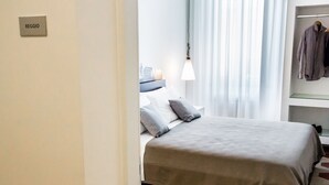 A hotel room with a bed, a nightstand, a lamp, and a clothing rack. - Rhegion B&B (Reggio Calabria)
