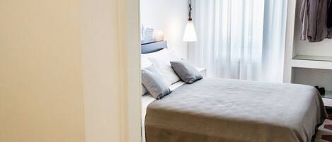 Una habitación de hotel con cama, mesita de noche, lámpara y perchero.