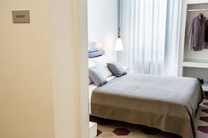 Quarto de hotel com cama, mesa de cabeceira, abajur e um cabideiro.
