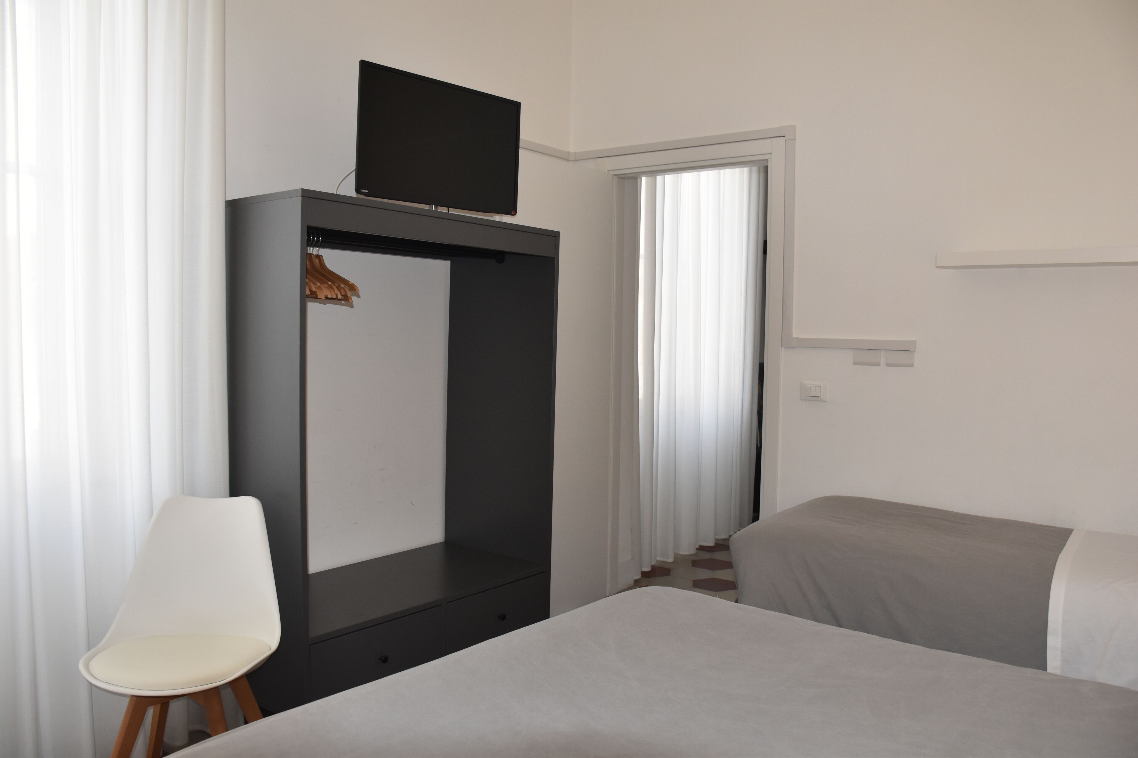 Quarto com uma cama, uma cadeira, um guarda-roupa e uma televisão em cima.
