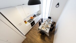 A modern kitchen with white cabinets, a dining table set for four, and a black pendant light. - Rhegion B&B (Reggio Calabria)