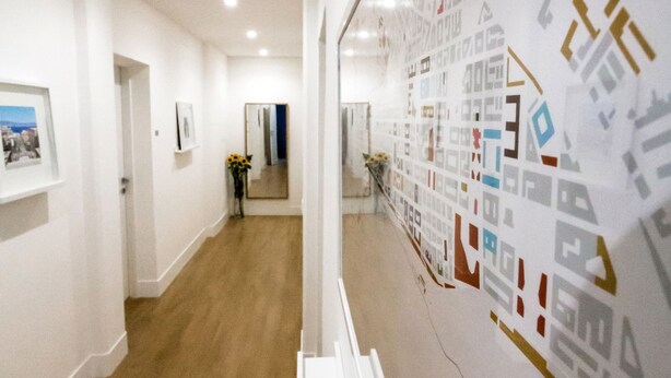 A hallway with a wooden floor, white walls, and a large map on the right. There are framed pictures on the left wall and a door at the end of the hallway. - Rhegion B&B (Reggio Calabria)