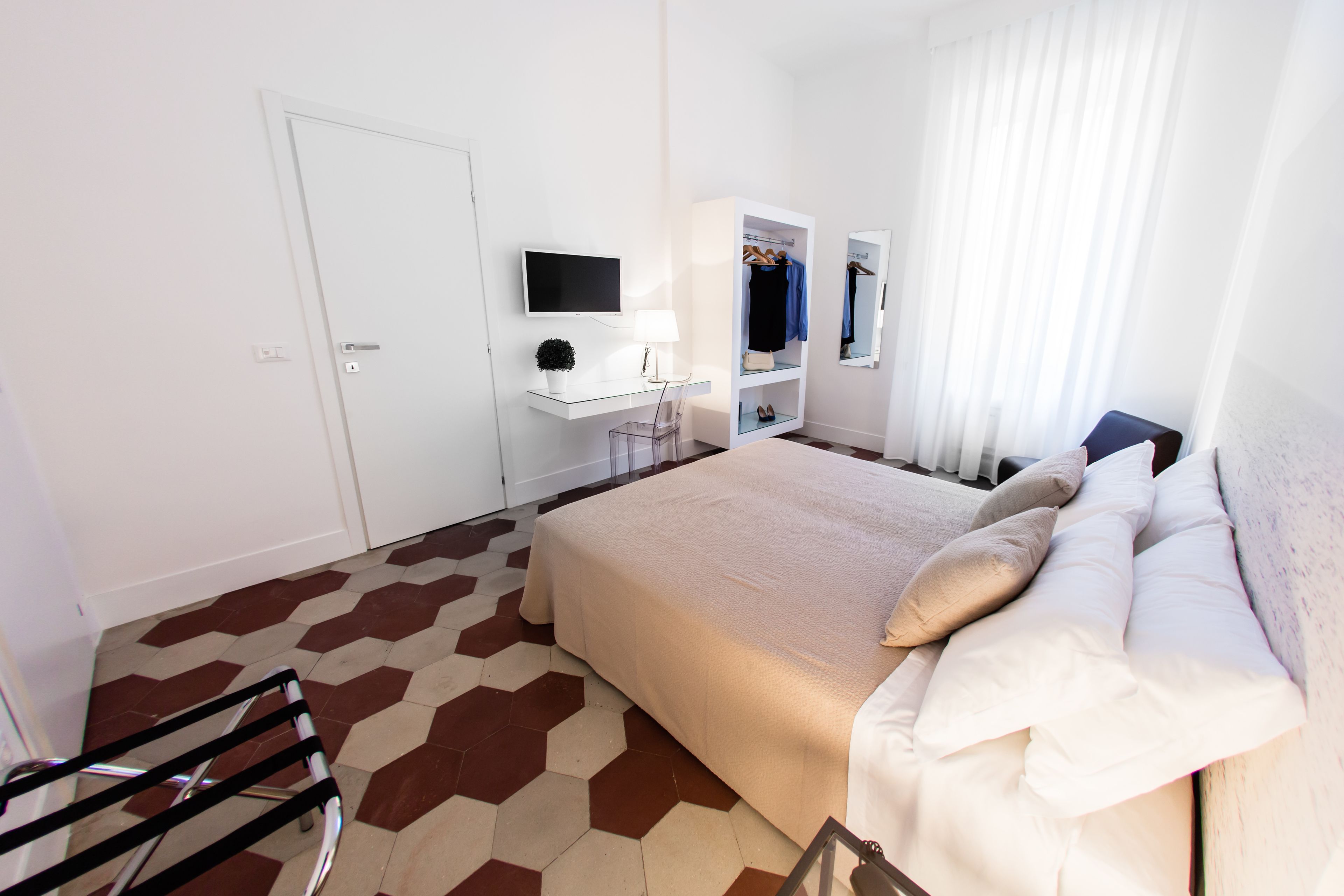 A hotel room with a bed, a desk with a computer, a TV, a mirror, and a wardrobe.