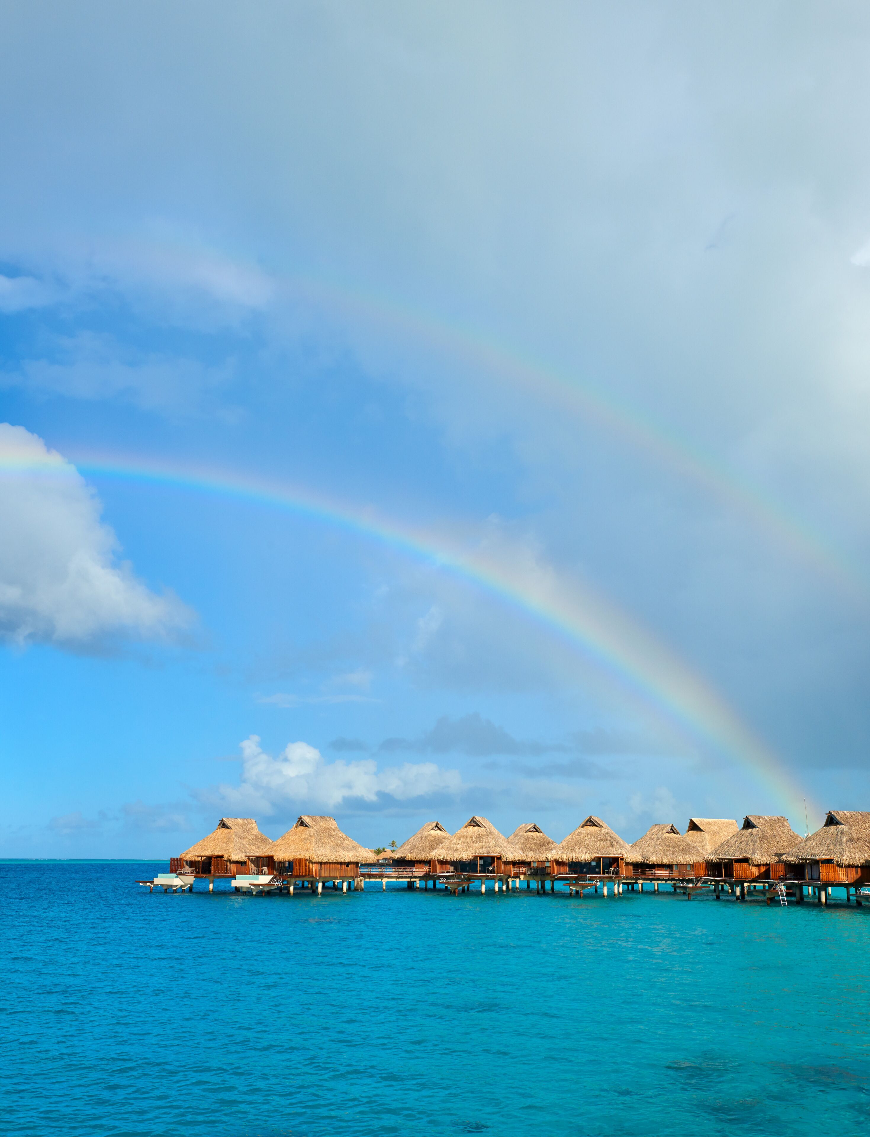Overwater bungalows with thatched roofs on stilts, connected by a wooden walkway over turquoise water.