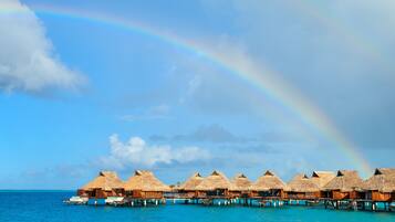 Overwater bungalows with thatched roofs on stilts, connected by a wooden walkway over turquoise water.
