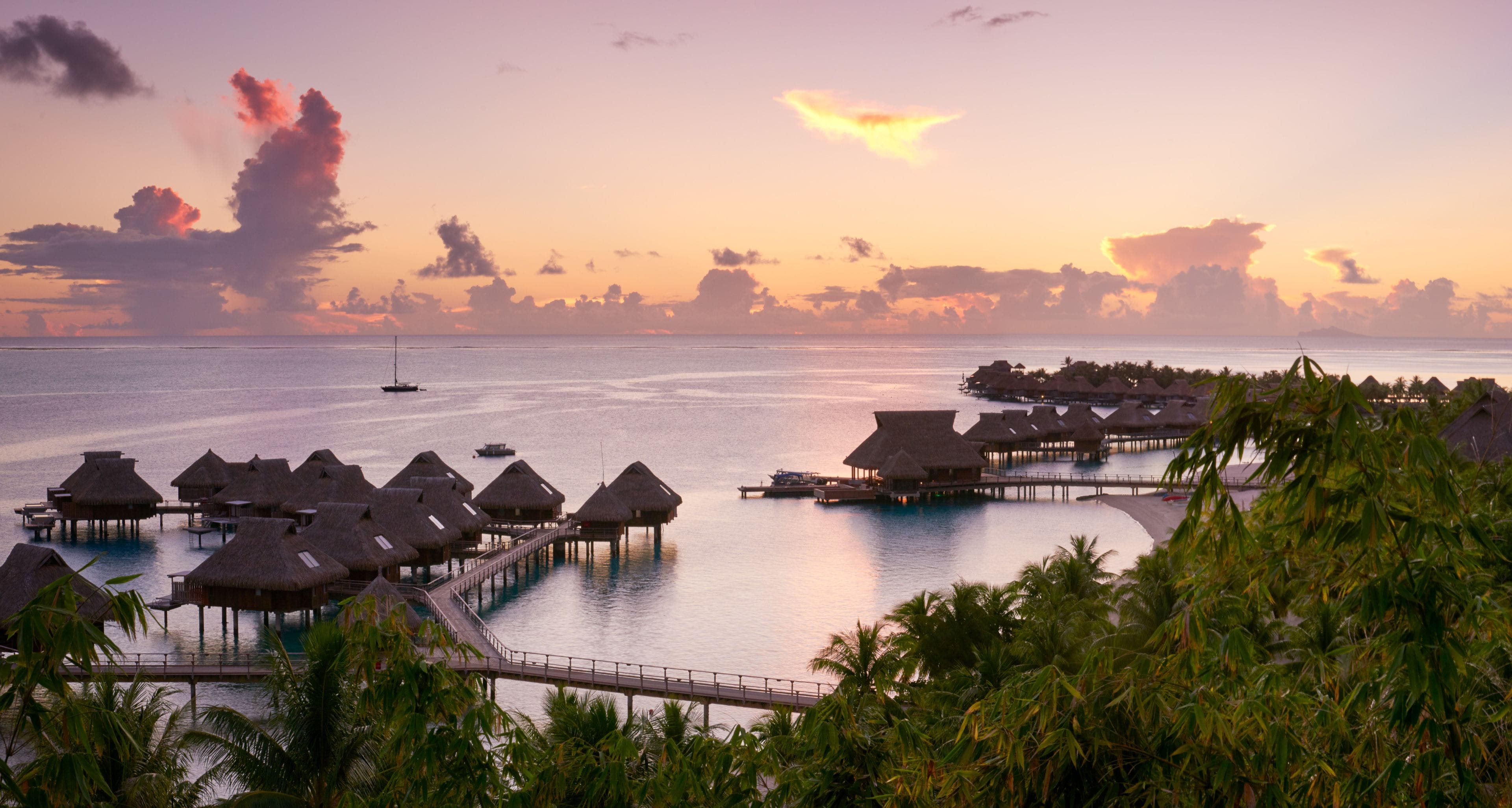 Overwater bungalows with thatched roofs, a pier, and a calm sea.