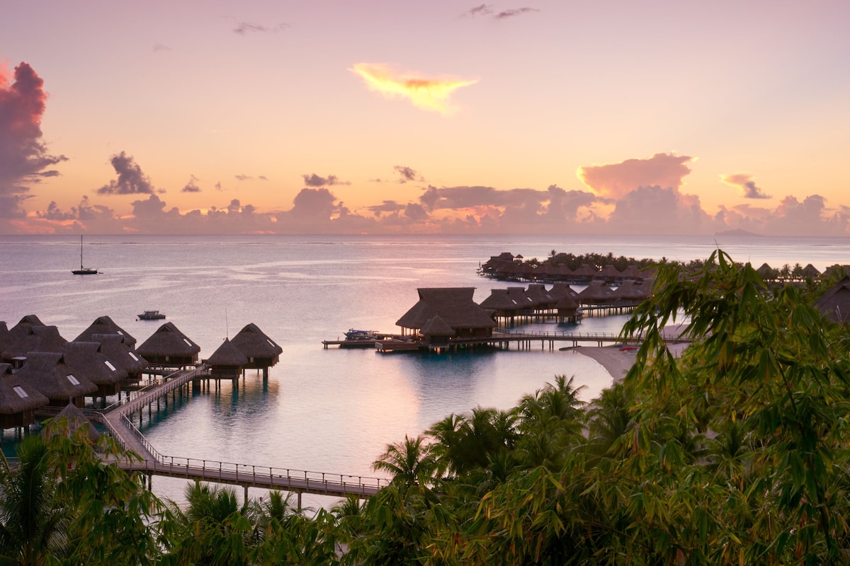Overwater bungalows with thatched roofs, a pier, and a calm sea.
