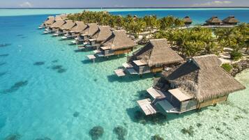Overwater bungalows with thatched roofs, clear turquoise water, and palm trees.