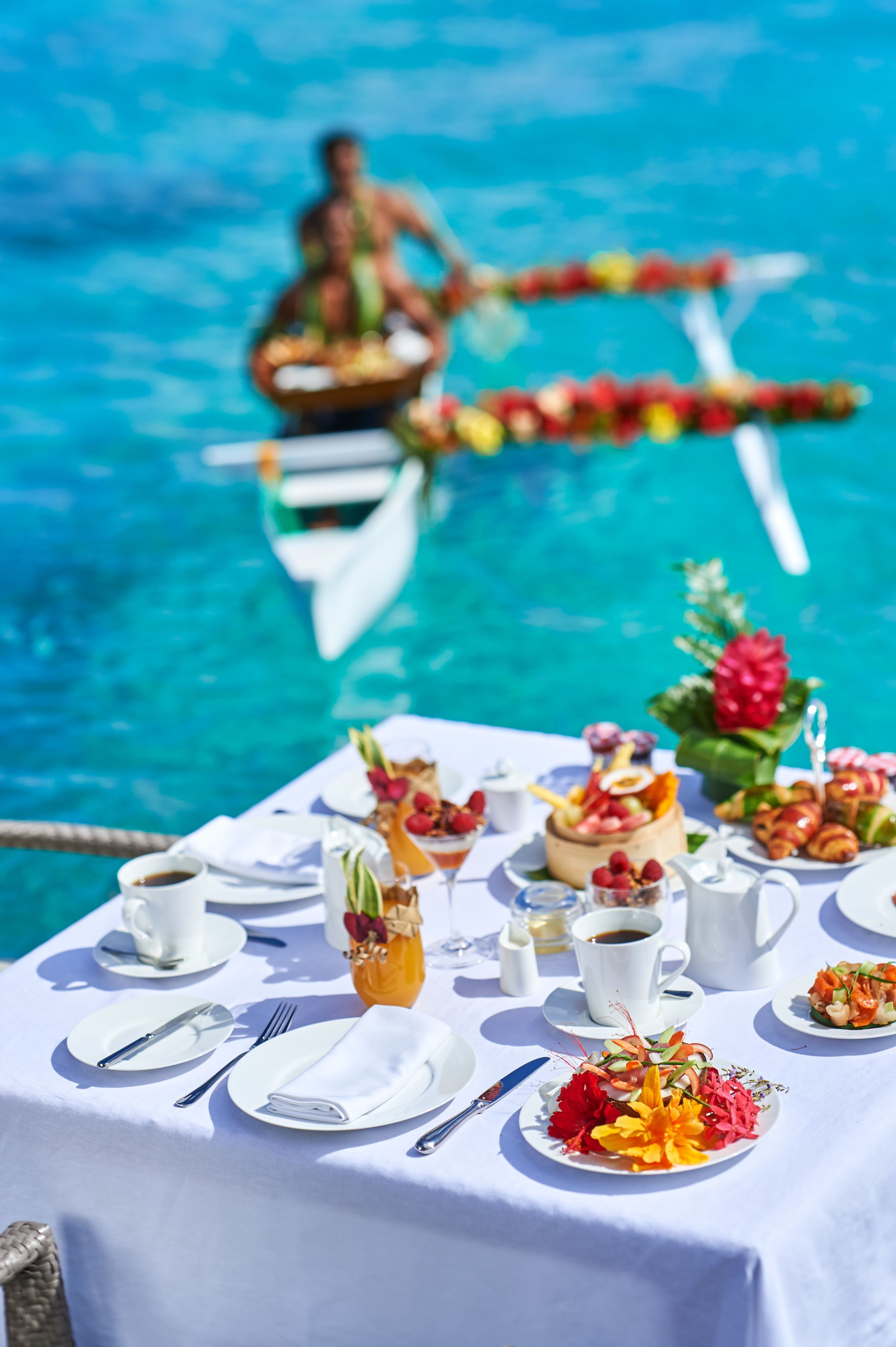 A table set for a meal with plates, cutlery, and a drink, overlooking a pool with a boat in the background.