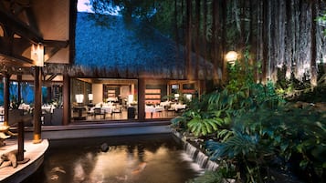 A restaurant with a thatched roof, indoor seating, and a koi pond.