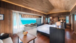 A hotel room with a large bed, a dining table, a small kitchen area, and a view of the ocean. - Conrad Bora Bora Nui (Bora Bora)
