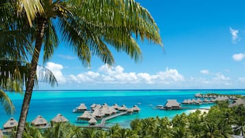 Una località turistica tropicale con bungalow sull'acqua, palme e acque cristalline color turchese.