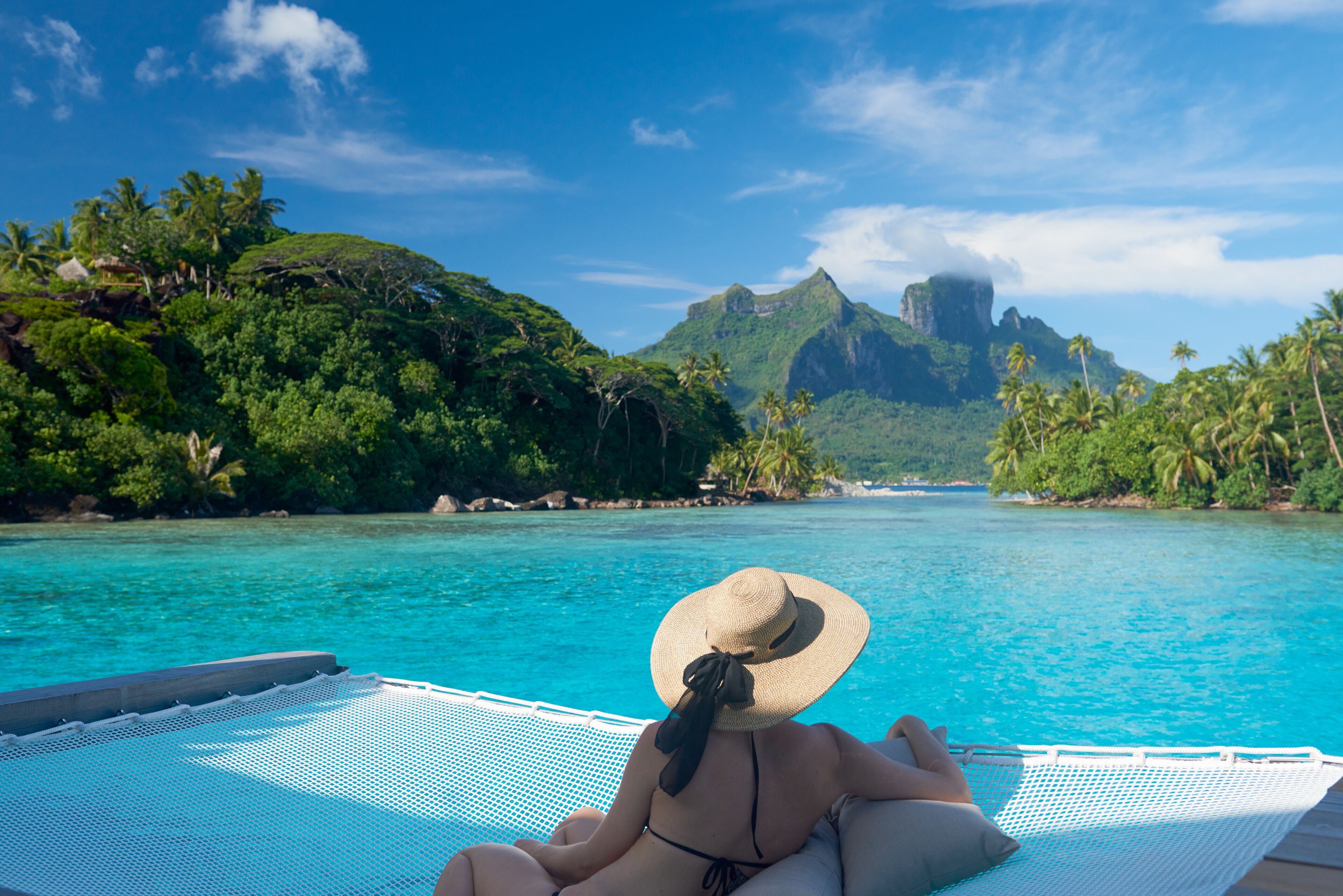 Una persona si rilassa su una poltrona a bordo piscina con vista su un paesaggio tropicale e montagne.