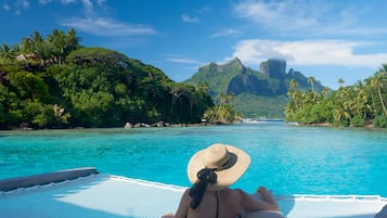 Una persona si rilassa su una poltrona a bordo piscina con vista su un paesaggio tropicale e montagne.