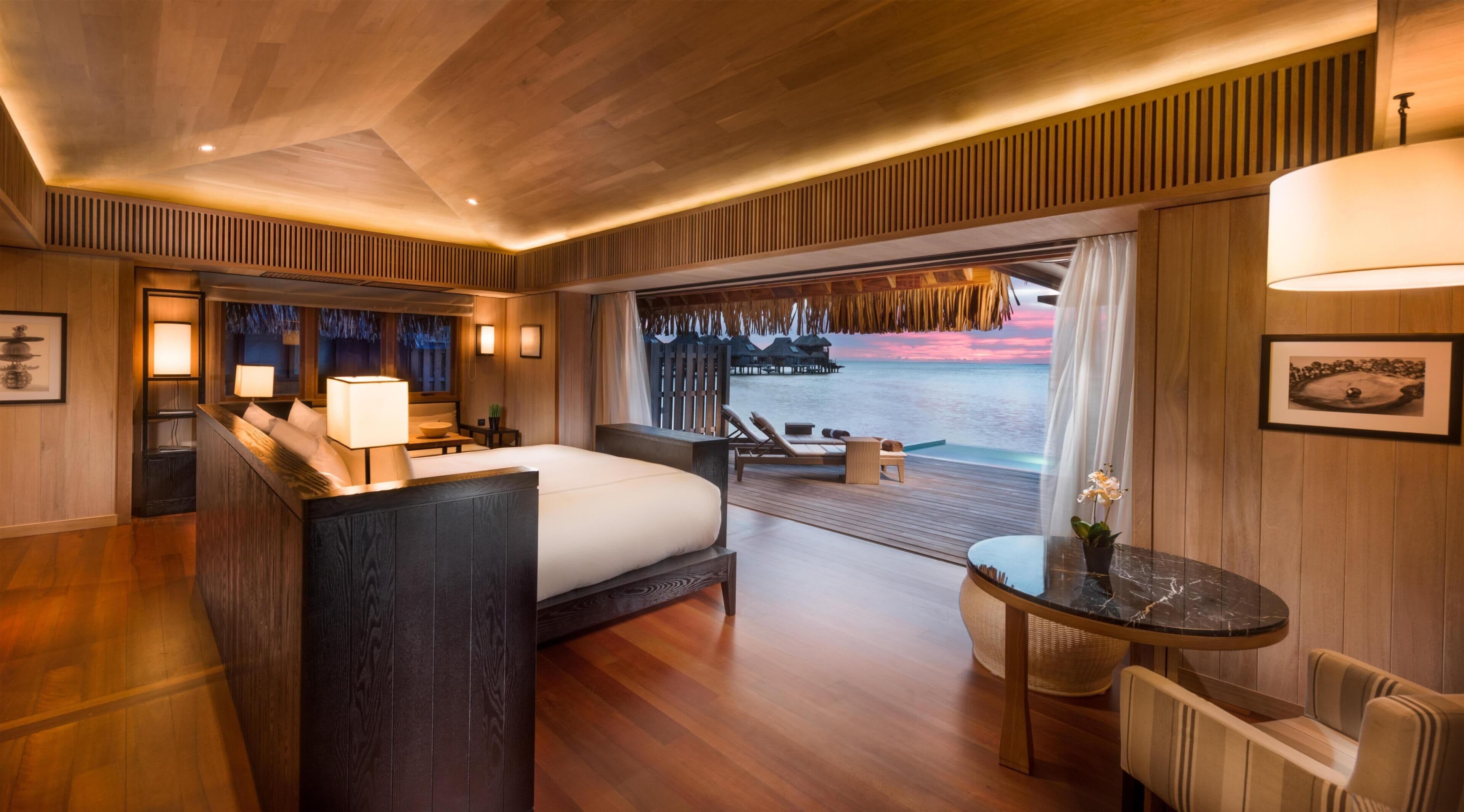 A room with a bed, bedside table, lamp, and a view of the ocean.