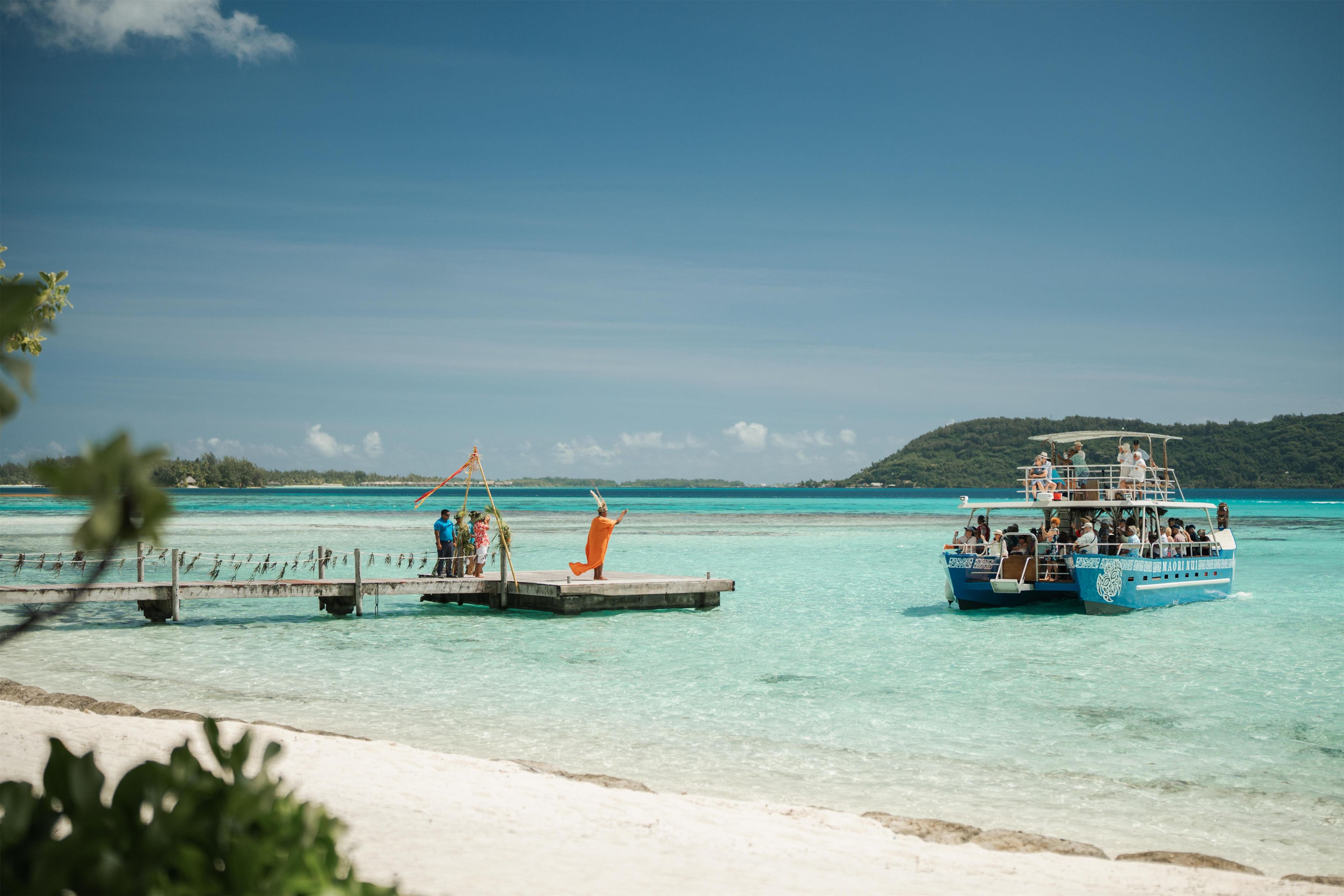A clear turquoise sea with a pier and a boat named 'MAORI NUI' with passengers.
