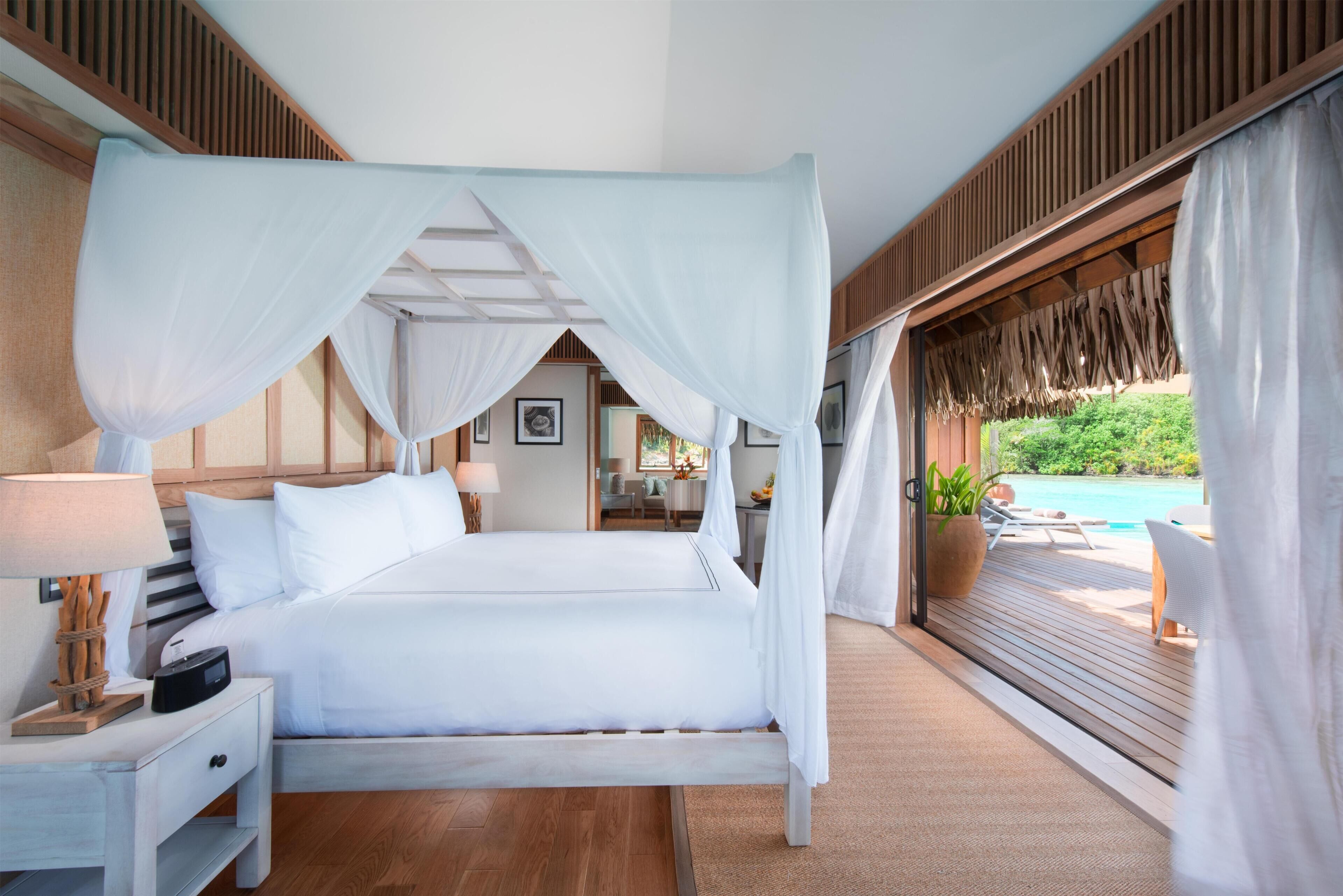 Un dormitorio con cama a dosel, una mesita de noche con lámpara y vista a una piscina.