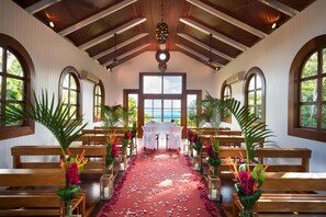 An interior with wooden benches, a red carpet, and large arched windows.