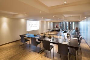 A conference room with a large screen displaying 'CONRAD BORA BORA NUI,' a long table with chairs, and a wooden floor.