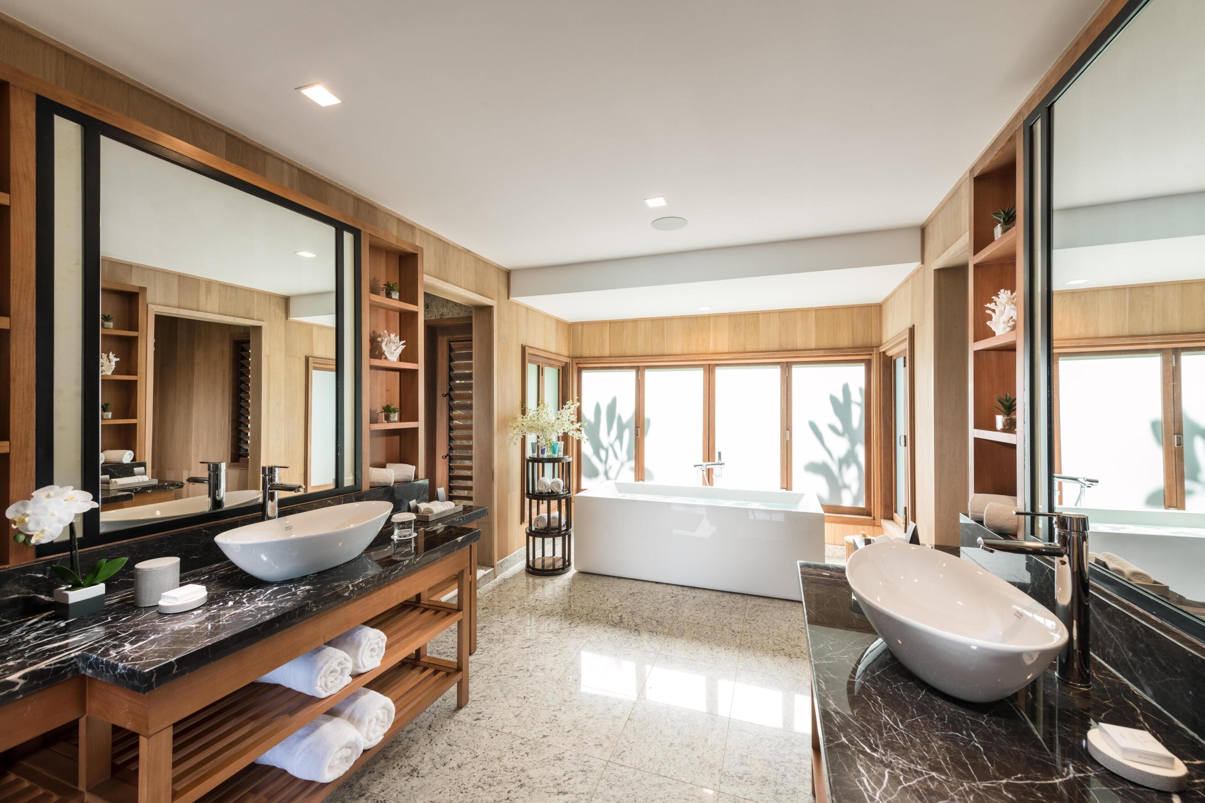 Un bagno moderno con un grande specchio, due lavabi, una vasca da bagno e scaffali in legno.