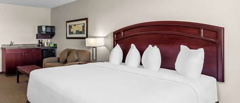 A hotel room with a large bed, a desk, a chair, a microwave, and a lamp.