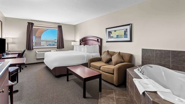 Une chambre d’hôtel comprenant un lit, un canapé, un bureau, une chaise, une petite table, une baignoire et une fenêtre avec des rideaux.