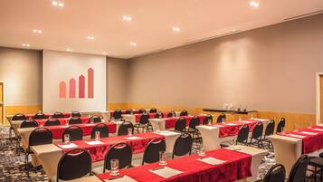 Un salón de conferencias con filas de mesas, cada una con mantel rojo, sillas negras y un atril al frente.
