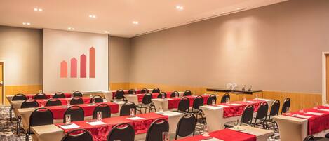 Un salón de conferencias con filas de mesas, cada una con mantel rojo, sillas negras y un atril al frente.
