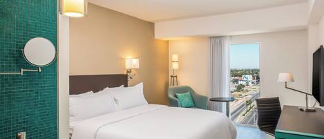 Habitación de hotel con una cama grande, un escritorio, una silla, un televisor, una ventana con vistas y un baño con espejo y lavamanos.