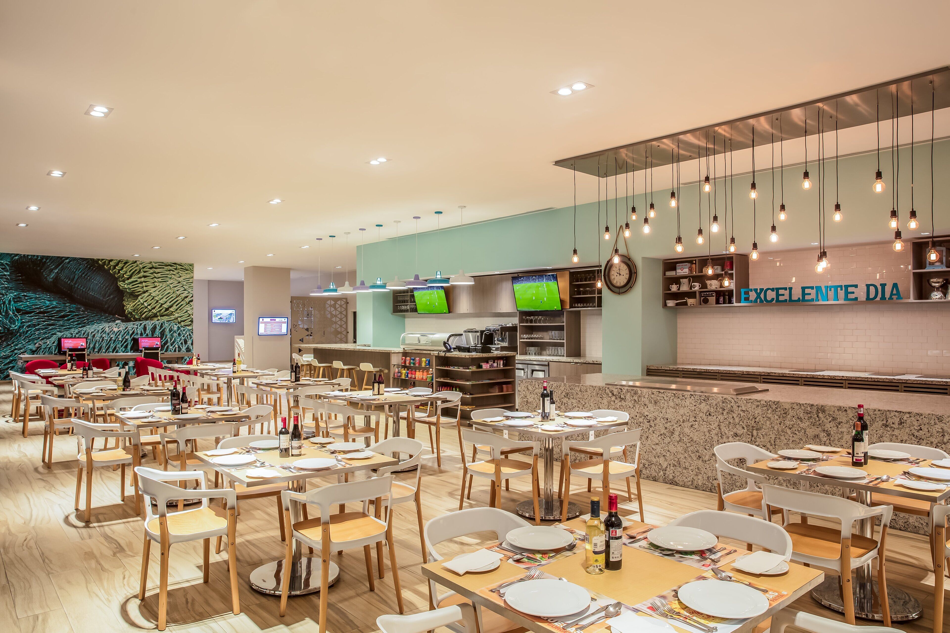 Un restaurant moderne doté de plusieurs tables et chaises, d’un espace cuisine et d’un comptoir sur lequel est affiché un panneau indiquant : « EXCELENTE DIA ».