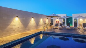 Zona de piscina con terraza de madera, sillas de descanso y sombrillas.