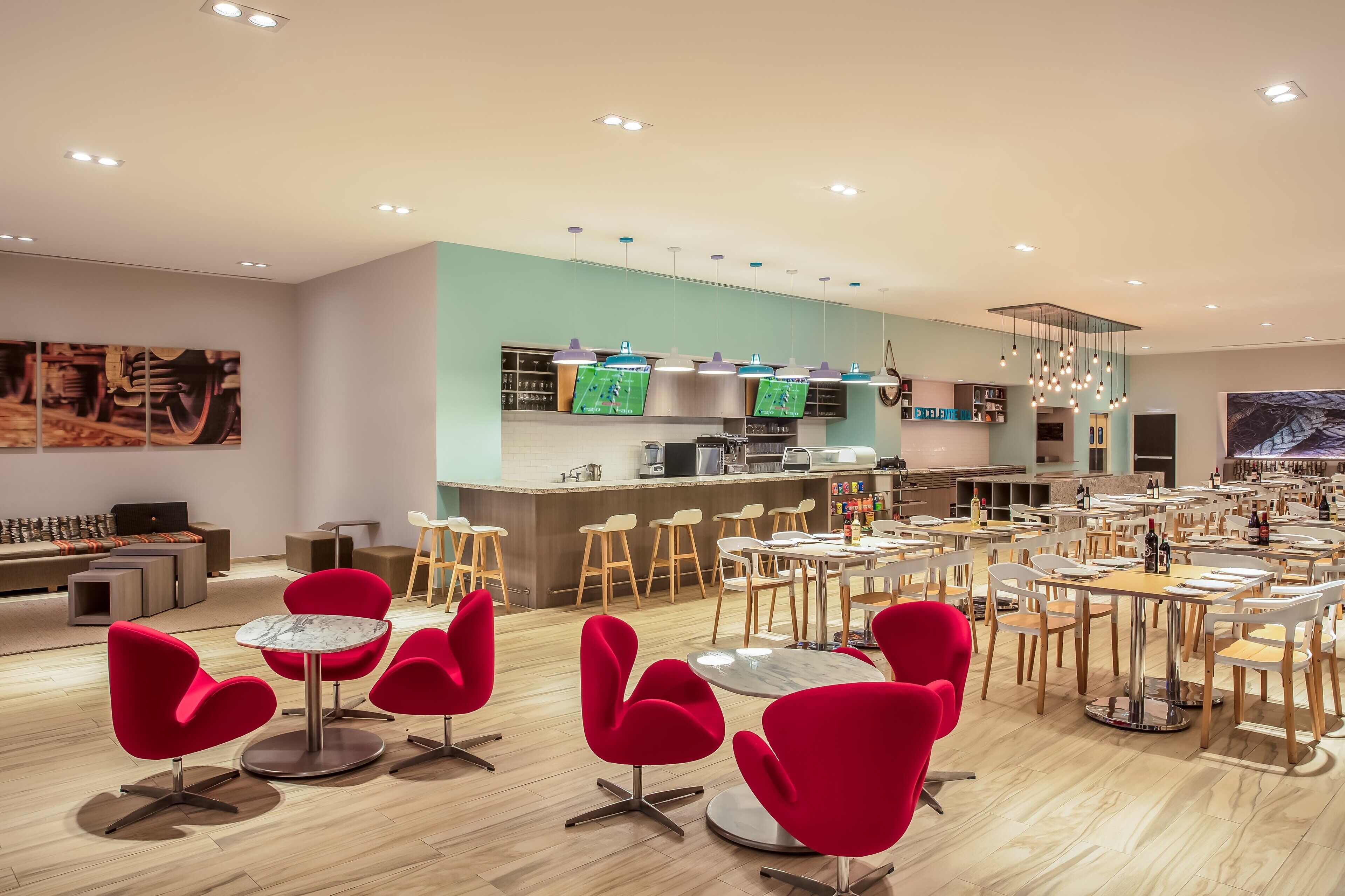 A modern restaurant with red chairs and tables, a kitchen area, and artwork on the walls.